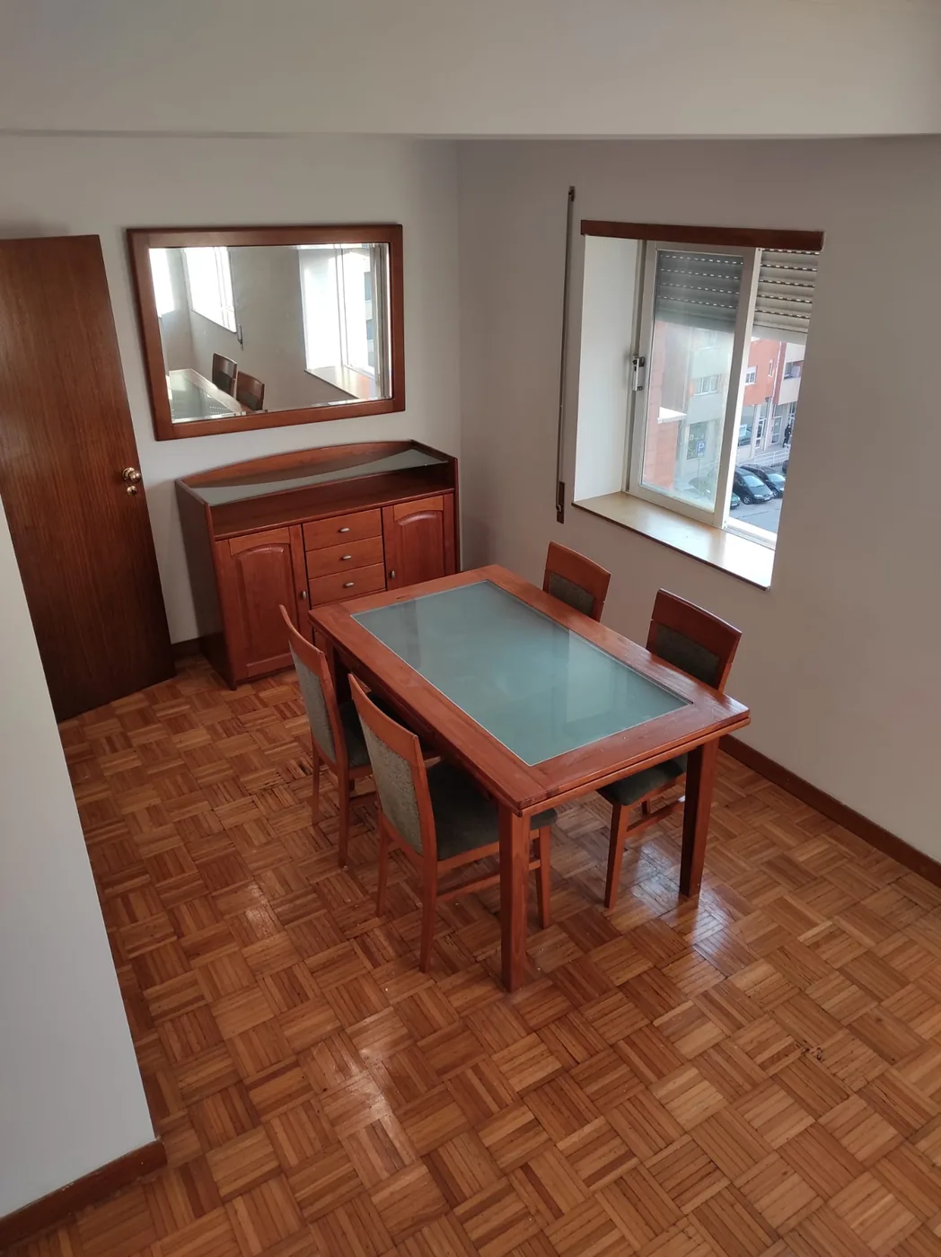 Zona de refeições do T3 com mesa, cadeiras, aparador em madeira e duas janelas