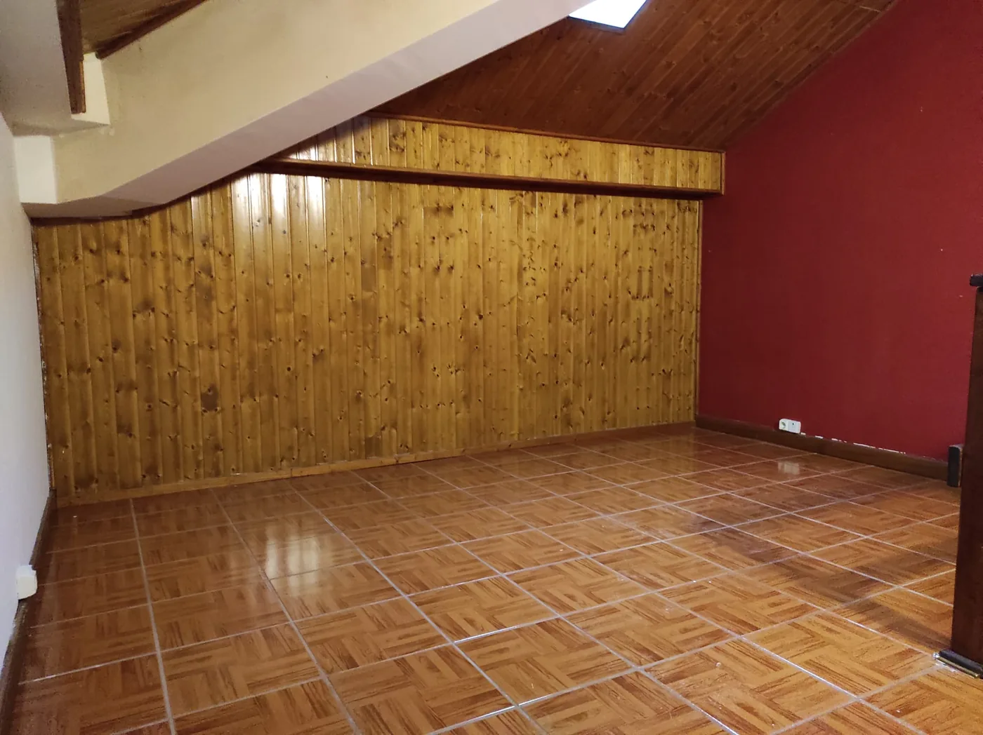 Sótão amplo do T3, com revestimento em madeira, tecto inclinado e uma parede pintada de vermelho